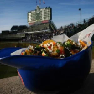 Ballpark nachos with stadium background and crowd.